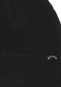 Black knit beanie with a textured pattern and a label sewn on side. The fabric appears warm and stretchy, suitable for cold weather.