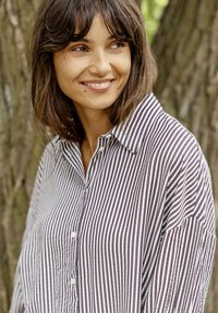 Striped button-up shirt in light brown and white, featuring a collar and loose fit. Textured fabric with visible seams. Soft and casual design.