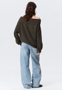 Overgrote donkerbruine off-the-shoulder trui, gestructureerde stof, brede mouwen, gecombineerd met lichtblauwe, losse spijkerbroek en zwarte schoenen.