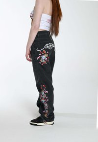 Pantalones vaqueros amplios negros con bordados de flores y calaveras a lo largo de las piernas, que presentan una cintura alta y una sutil textura deslavada.