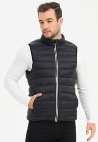 Gilet en doudoune noire avec un col haut, fermeture éclair à l'avant et poches latérales ; présente une texture matelassée et un design élégant et ajusté.