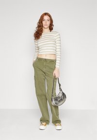 Crop top bej cu dungi, pantaloni cargo verzi măslin, geantă argintie și adidași albi cu accente galbene. Croială dreaptă și material texturat.