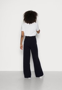 Lange navyblauwe broek met een hoge taille, gecombineerd met een witte t-shirt met korte mouwen. Zachte stof en een ontspannen pasvorm, getoond vanuit de achterkant.