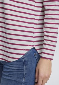 Stribet langærmet top i hvid og fuchsia, med buet kant og sideslids. Sat sammen med denimjeans, der viser stofets tekstur og mønster.