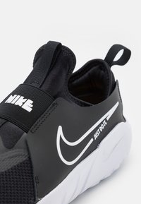 Černé nazouvací tenisky s síťovinovým svrškem, elastickým páskem s logem "Nike", tónovým designem a bílou podrážkou s textem "Just Do It".