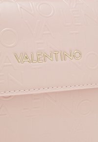 Ljusrosa handväska med präglat logomönster. Har en guldfärgad "VALENTINO" namnskylt och diskreta sömnadsdetaljer. Slät, glänsande yta.