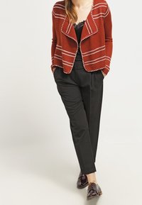 Karidgan rezavě červené barvy s bílými pruhy, otevřený přední díl, kombinovaný s černými kalhotami na míru a hnědými oxfordkami. Pletenina s texturou.