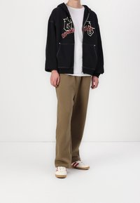 Sweat-shirt à capuche noir avec des lettres rouges et blanches, assorti à un pantalon beige ample et des chaussures blanches avec des rayures rouges.