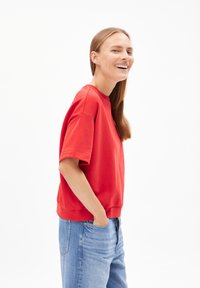 Roter Baumwollpullover mit rundem Halsausschnitt und kurzen Ärmeln, kombiniert mit hellblauen Jeans. Glatte Textur, lässige Passform.