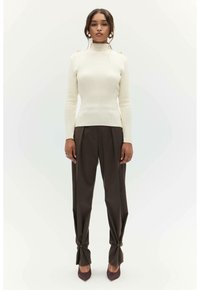 Crème ribbed coltrui met gouden schouderknopen, gecombineerd met hooglopende donkerbruine pantalon met knoopaccenten en puntige hakken.