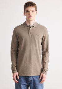 Polo de manga longa em algodão castanho claro, com gola abotoada e bordado discreto do logo no peito. Ajuste casual com punhos canelados.