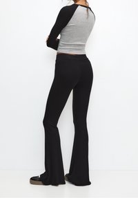 Pantalon évasé noir côtelé associé à un haut à manches longues gris et noir ; tous deux ajustés avec une texture lisse et des couleurs contrastées.