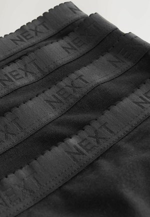 Tessuto elastico nero con tre bande orizzontali che presentano il testo in rilievo "NEXT". Texture liscia con dettagli ondulati ai bordi.