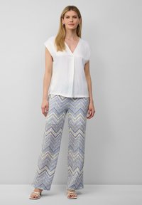 Blouse blanche à manches courtes avec un col en V, associée à un pantalon large à motif zigzag multicolore en bleu, jaune et crème.