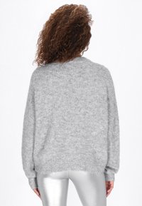 Overdimensioneret grå sweater, tekstureret stof, ribbede ærmer og bund. Båret med skinnende sølvleggings, vist fra ryggen.