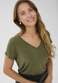 Olieti zaļa īsais piedurkņu V veida krekls, kas izgatavots no mīksta auduma. Minimalistisks dizains ar gludu tekstūru un brīvu piegulšanu.