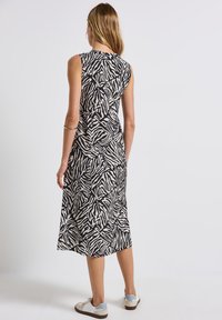 Sleeveless black and cream dress featuring a zebra print with a mid-length cut. Paired with white sneakers, showcasing a relaxed fit.
