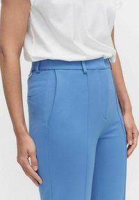 Skräddarsydda blå byxor gjorda av ett mjukt tyg. Har en slät front, sidofickor och en smal passform med bälteshällor.