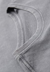 Camiseta de algodón gris con cuello redondo, que presenta una textura suave y detalles de costura sutiles. La tela tiene un aspecto ligeramente desvanecido.