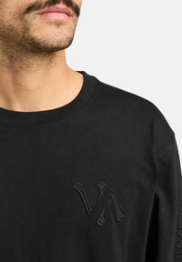 Zwarte long sleeve shirt met een ronde hals en geborduurd logo op de borst. Zachte katoenen stof met een gladde textuur.
