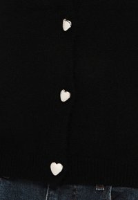 Μαύρη πλεκτή ζακέτα με πέντε ασημένια κουμπιά σε σχήμα καρδιάς κατά μήκος του μπροστινού μέρους, με ριμπ τελείωμα και μαλακή υφή.