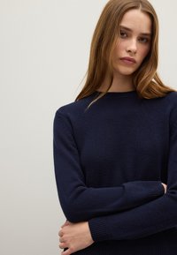 Dunkelblaues Strickpullover mit rundem Ausschnitt, gerippten Bündchen und einer strukturierten Oberfläche. Der Schnitt ist slim, mit langen Ärmeln und einem weichen Erscheinungsbild.