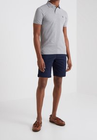 Polo shirt grigia a maniche corte con colletto, abbinata a pantaloni corti blu scuro e scarpe da barca marroni. Design casual con vestibilità rilassata.