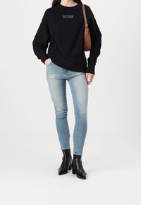 Svart sweatshirt med "BOSS"-logotyp, bärs med ljusblå smala jeans och svarta klackstövlar. Enkel design, avslappnad passform, minimal detaljering.