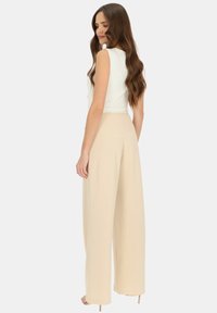 Kremowa bluzka zestawiona z beżowymi, wysokotaliowymi spodniami o szerokich nogawkach. Tkanina wydaje się gładka z delikatnym połyskiem, prezentując czyste linie i dopasowany krój.
