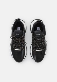 Sneaker sportive nere con tomaia in rete e lacci dai colori arcobaleno. Suola bianca con dettagli testurizzati. Etichette visibili sulle linguette delle scarpe.