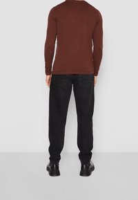 Chemise à manches longues marron foncé au design ajusté, associée à un pantalon en denim noir avec poches arrière et coupe droite. Des chaussures noires complètent le look.