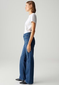 Wijd gesneden blauwe jeans van denim, met een hoge taille en schone achterzakken. Gecombineerd met een eenvoudig wit T-shirt en zwarte schoenen.