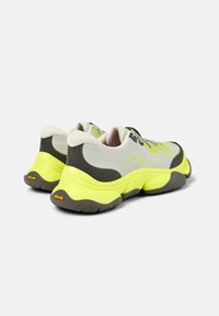 Pár šedých a neonově žlutých sportovních tenisek s tlustou podrážkou a černou Vibram podrážkou, zobrazených zezadu a pod úhlem.