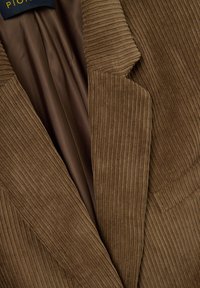 Bruine corduroy blazer met verticale ribbels, scherpe revers en een gladde voering. Opvallende stiksels langs de randen.