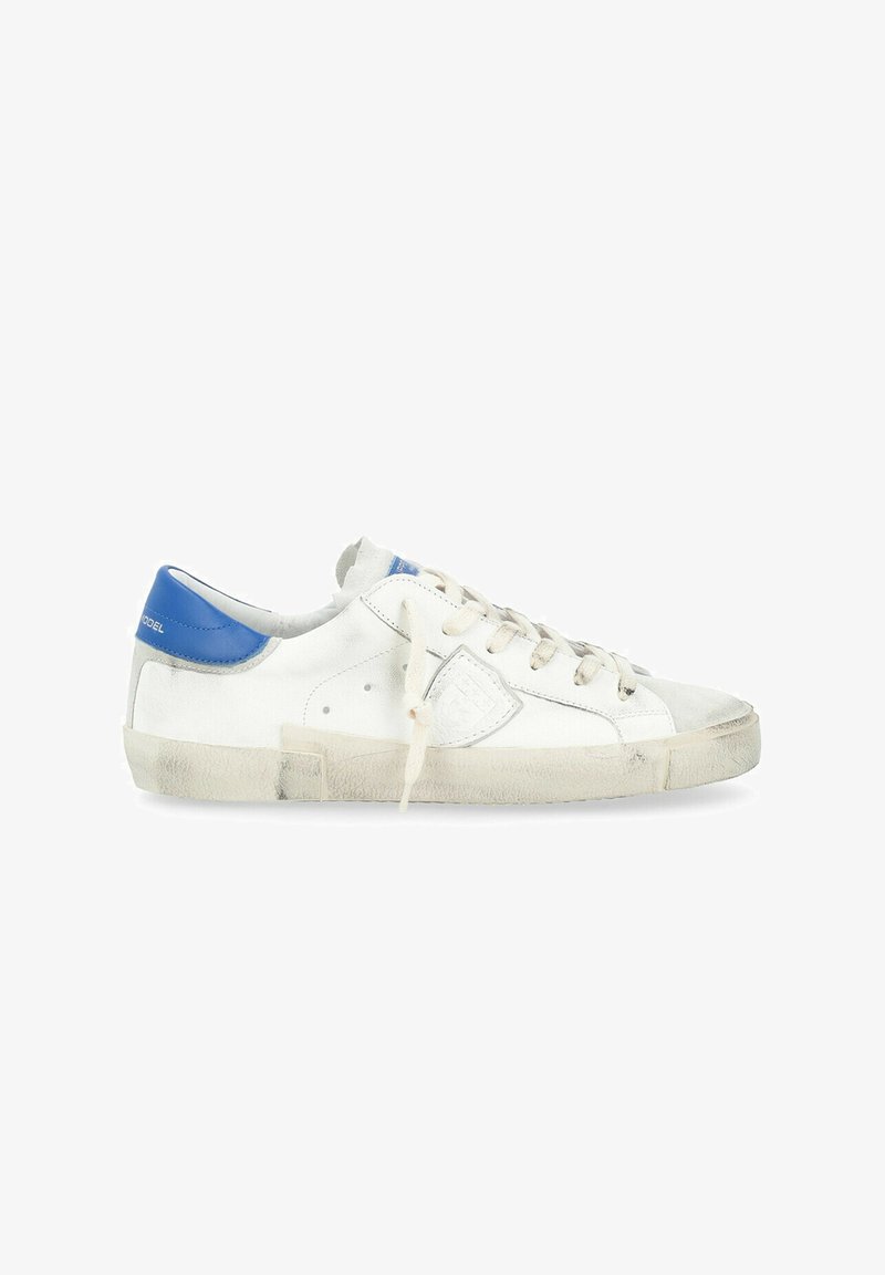 Baskets blanches en cuir avec des accents bleus, semelles texturées et lacets beiges. Présentent un écusson logo et un bout usé. Design décontracté.