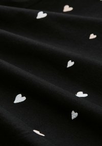 Czarny materiał o gładkiej teksturze, z haftowanymi sercami w białym i jasnoróżowym kolorze, rozsianymi po powierzchni.
