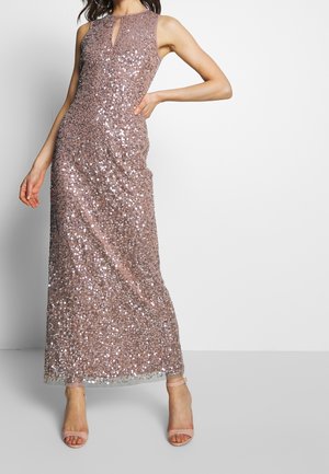 Bez rękawów wieczorowa sukienka w kolorze mauve z cekinami, dekoltem z wycięciem, dopasowaną talią i beżowymi szpilkami z paskiem wokół kostki na stojącej kobiecie.
