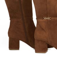 Brown suede ankle boots with a square block heel, side zipper, and gold-tone hardware accent. Smooth texture with a fitted design.
