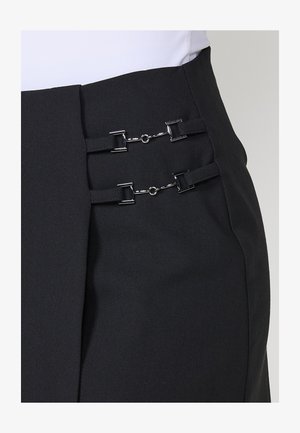 Svart kjol med skräddarsydd design och två silverklämsor framtill, tillverkad av ett slätt tyg med en lätt lyster.