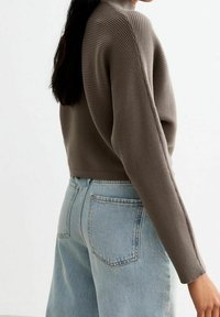 Brown ribbed knit sweater with a high neck, paired with light blue high-waisted jeans featuring back pockets and a relaxed fit.