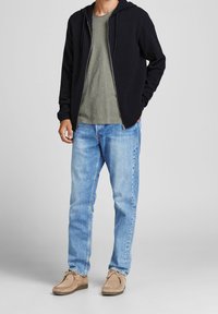 Black zip-up hoodie, olive green t-shirt, light blue jeans, and brown suede shoes with laces. Smooth texture, casual fit.