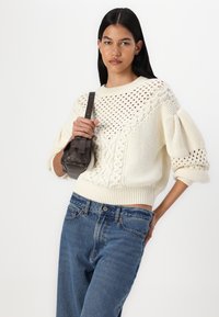 Pull en maille épaisse crème avec un motif ajouré, manches chauve-souris et ourlet côtelé, associé à un jean en denim bleu taille haute.