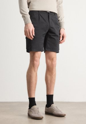 Black cotton shorts with pockets, featuring a straight cut and belt loops. Worn with gray shoes and dark socks. Smooth texture.
