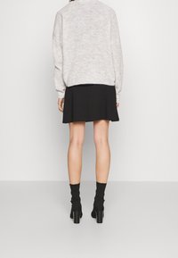 Světle šedý pletený svetr s volným střihem, zkombinovaný s černou rozšířenou sukní. Modelka má na sobě černé ponožkové podpatky. Zádový pohled s hladkými texturami.