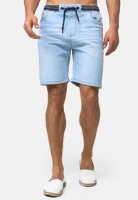 Lys blå denimshorts med snøring i midjen, sidelommer og brettede kanter, synlig sømdetalj og en avslappet passform.