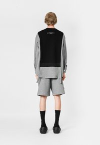 Conjunto masculino que incluye una sudadera con capucha negra y gris con largas aberturas laterales, combinada con pantalones cortos grises y calcetines negros hasta el tobillo.