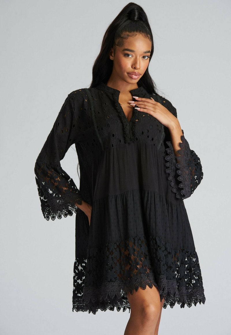 Zwarte jurk met broderie anglaise details, een geplooide corsage en geschulpte kantafwerking bij de mouwen en zoom. Zacht, lichtgewicht stof.