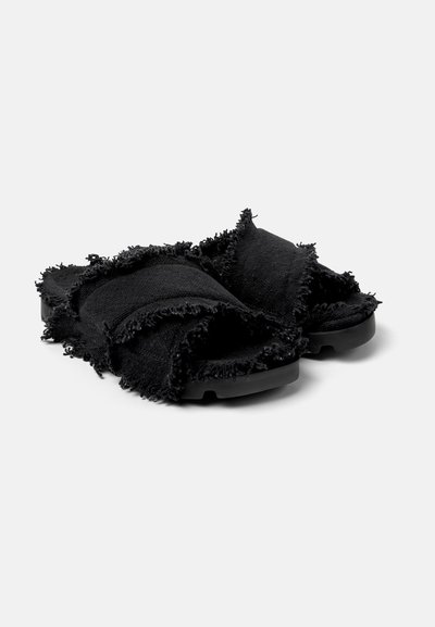 Svarta slide-sandaler med texturerade, fransiga tygremmar, med en dämpad sula och rundad form. Ingen synlig hårdvara eller ytterligare detaljer.