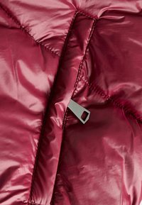 Bordeaux pufferjack met een gladde, glanzende buitenkant, gequiltte secties en een metalen rits met een rechthoekige uitsparing.