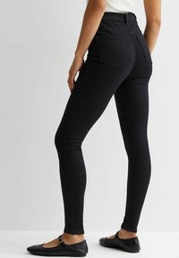 Jeans skinny de cintura alta en negro, fabricados con denim elástico. Presenta dos bolsillos traseros y un acabado liso y elegante. Combinados con bailarinas negras.